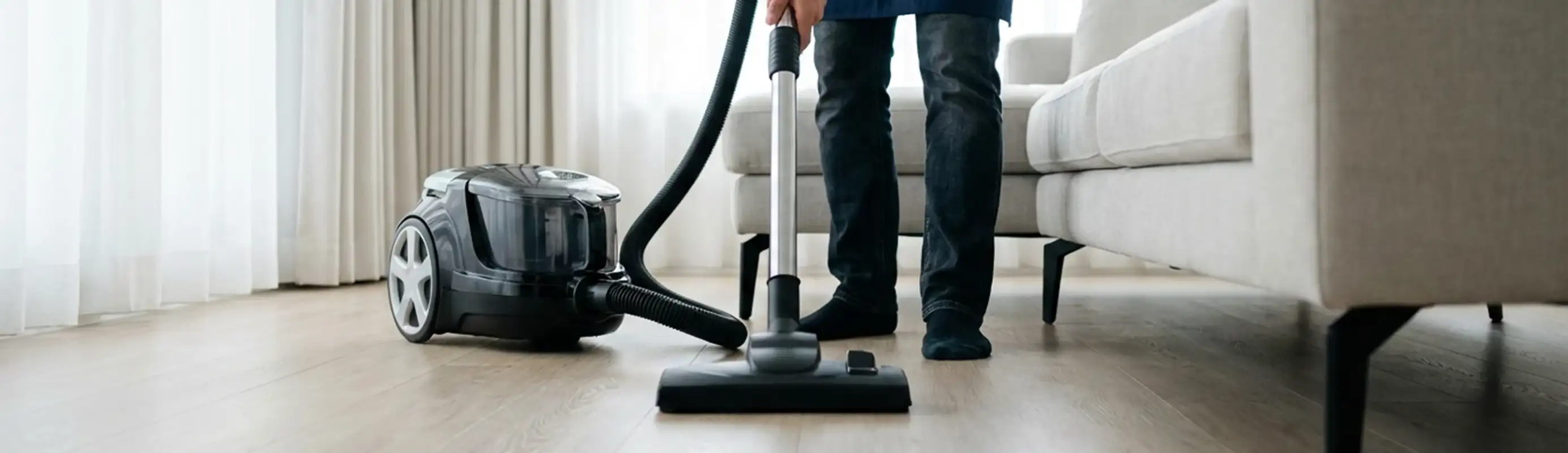 Professional house cleaner vacuuming a living room floor with a canister vacuum cleaner, Fort Worth, TX.