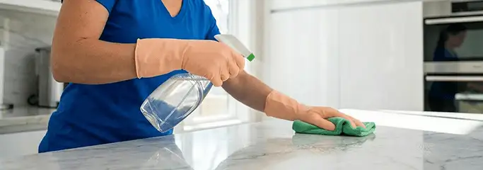 Maid service worker spraying and wiping a kitchen countertop with a microfiber cloth for sanitizing, Fort Worth, TX.