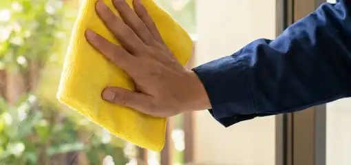 House cleaner wiping a glass window with a yellow microfiber cloth for streak-free cleaning, Fort Worth, TX.